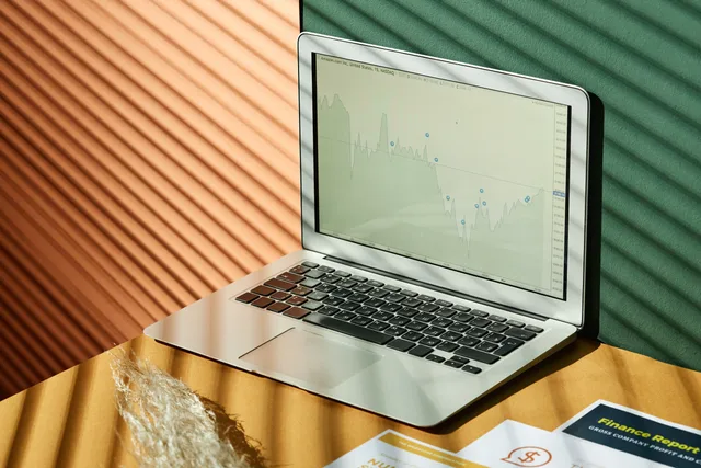 A laptop displaying analytics with financial papers on a textured surface, captured in warm lighting. System WMS w małym sklepie: kiedy wdrożenie ma sens?